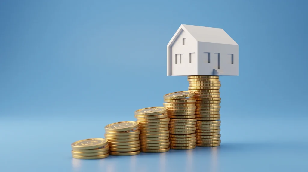A small white house model resting on stacks of gold coins representing savings.