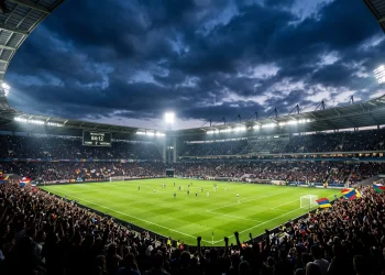A professional football stadium illuminated by floodlights during a night match.