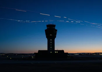 A conceptual silhouette of an air traffic control tower under a dark sky with broken light trails representing flight disruption.