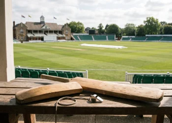 A cricket bat and coaching equipment resting on a bench overlooking a pitch.