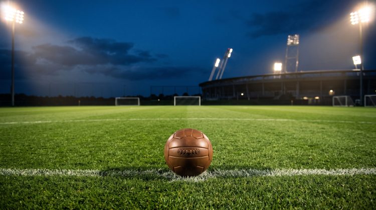 A football on a stadium pitch under bright lights at night.