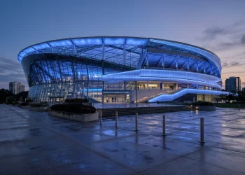 A large tennis stadium glowing in blue light at night as a memorial tribute.