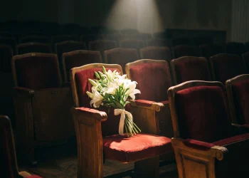 A spotlight on an empty theater chair with lilies.