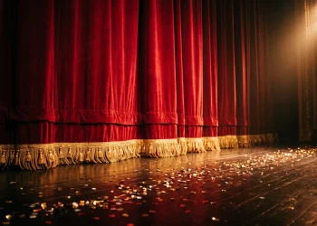 A dramatic red velvet stage curtain under bright studio spotlights with sparkling sequins on the floor.