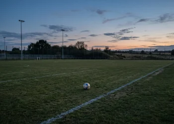 A solitary football sits on the edge of a quiet training field.