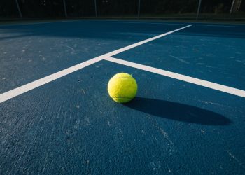 A tennis ball on a blue hard court at night under stadium lights